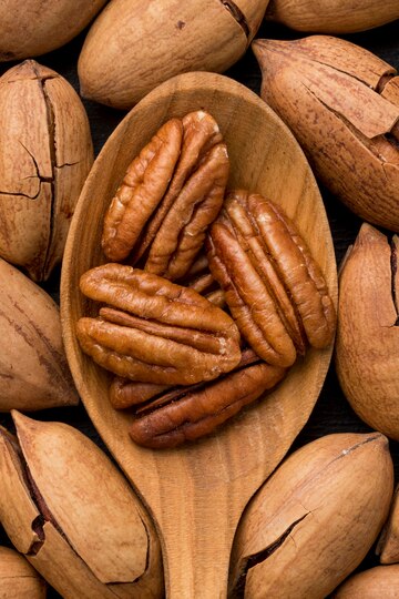 Pecan halves on a wooden spoon surrounded by pecans in the shell
